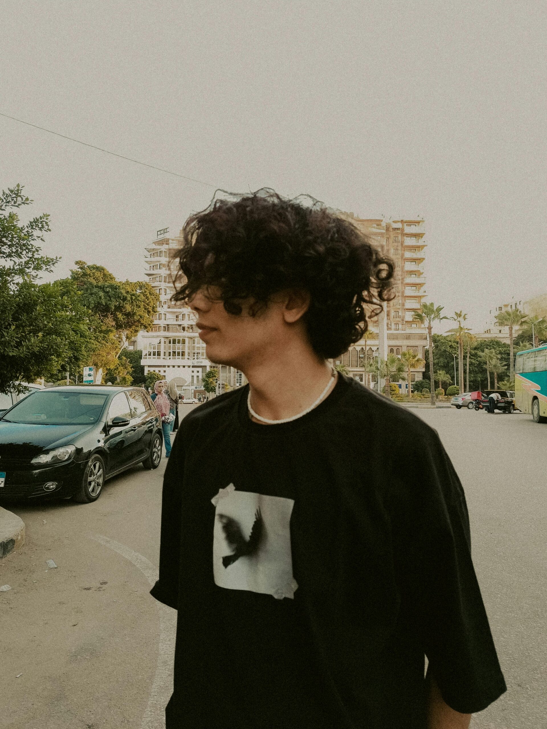 Young man with curly hair standing in Alexandria, Egypt street scene.